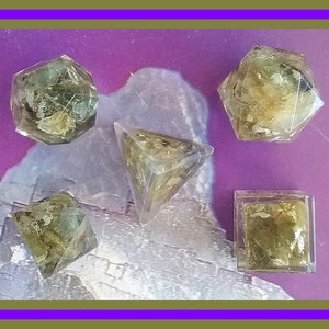 May include: Set of five clear resin dice with green and gold flecks. The dice are in the shapes of a pyramid, a cube, and a dodecahedron.