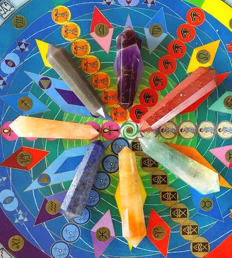 May include: Seven double-terminated crystal points in purple, red, orange, yellow, green, blue, and gray arranged in a circular pattern on a colorful circular board featuring various symbols, zodiac signs, and geometric shapes.