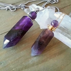 Op de afbeelding: Twee amethistkristal hangerkettingen met gouden en zilveren kettingen. De hangers zijn gevormd als lange, puntige kristallen met een ronde amethist edelsteen aan de bovenkant.