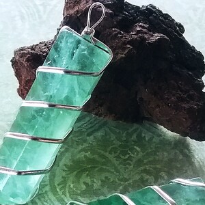 May include: A green fluorite crystal pendant wrapped in silver wire. The pendant is approximately 5 cm long and is a beautiful shade of green.