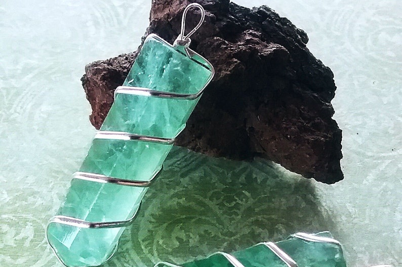 May include: A green fluorite crystal pendant wrapped in silver wire. The pendant is approximately 5 cm long and is a beautiful shade of green.