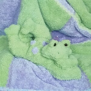 May include: A craft pattern for a bean bag baby and quilted blanket. The blanket is green and purple with a frog design. The text "L.A. Designs" and "Tadpole" are visible. The pattern number is 3084.