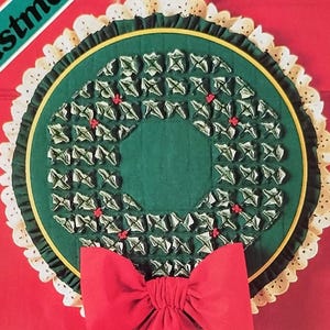 May include: A Christmas-themed craft pattern by Yours Truly. The cover features a green wreath with red accents and a large red bow. The text "Christmas" is visible. The pattern includes instructions for hoop wallhanging or vest in three sizes.