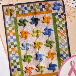 May include: A quilt pattern cover featuring a colorful pinwheel design. The cover includes the text "Flying Pinwheels-Baby Style" and "Cookie's Creations". The quilt design incorporates various colors, including blue, green, orange, and yellow.
