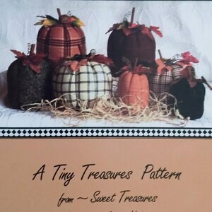 May include: A sewing pattern titled Lil Punkins by Amber Hiebert for Sweet Treasures. The cover features a photograph of six fabric pumpkins in various plaid and solid colors, ranging from 6 inches to 10 inches in size, with stems.