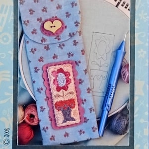 May include: A blue floral fabric punchneedle tool holder with a heart-shaped button closure. The holder features a floral design and the text "PUNCHNEEDLE TOOL HOLDER". Finished size is 3.25" x 8.5".