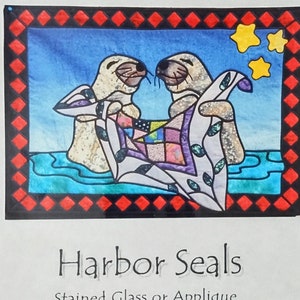May include: A pattern for a stained glass or applique project titled "Harbor Seals." The image features two seals holding a quilt with colorful patches, set against a blue background with yellow stars. The border is red and black.
