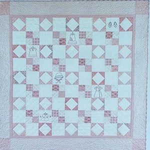 May include: A pink and white baby quilt with a patchwork design. The quilt features embroidered images of baby clothes and accessories. The text "Bunny Hill Baby" and "All Dressed Up" are also visible.
