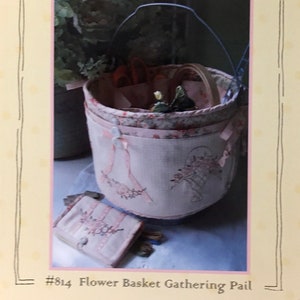 May include: A pink and white fabric flower basket with a metal handle, featuring floral embroidery and ribbon accents. A matching small case is also visible. The text "Crabapple Hill" and "Flower Basket Gathering Pail" are displayed.