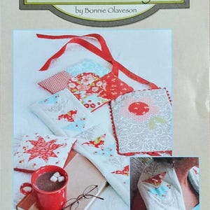 May include: Image of a product package with the text "Cotton Way" and "Soothing Hot/Cold Rice Bags." The image displays various patterned rice bags in red, white, and blue, along with a red mug of hot chocolate, a book, and eyeglasses.