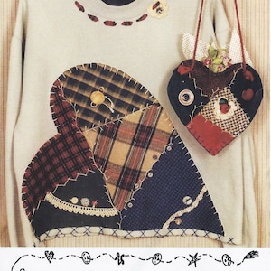May include: A beige sweatshirt with a large patchwork heart design in plaid and navy fabrics. A matching heart-shaped purse hangs from the side. The design includes old lace and buttons. The text "Caught Up in Stitches" is at the bottom.