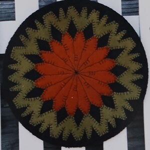 May include: A framed image with the text "Easter Veggies" and "Wooden Spool Designs." The image features a black and orange circular design, a black bunny with a carrot, and a white picket fence.