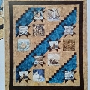 May include: Two quilt patterns titled "Wilderness Trails" are displayed. The larger quilt features a tan background with blue zigzag patterns and small square images. The smaller quilt mirrors the design. The text "Lighthouse Quilts & Things" is visible.