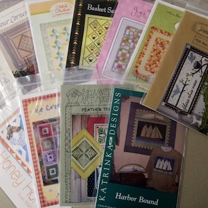 May include: A collection of quilting patterns in plastic sleeves. The patterns feature various designs, including geometric shapes, floral motifs, and nautical themes. Titles include "Four Corner," "Ice Cream," and "Harbor Bound."