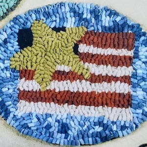 May include: A round, handmade rug with a patriotic theme. The rug features a star and stripes design, with a blue border. The star is yellow, the stripes are red and white, and the border is blue.