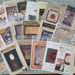 May include: A collection of Christmas-themed quilting patterns in clear plastic sleeves. The patterns feature various designs, including Christmas trees, Santa Claus, and festive wreaths. The color palette includes red, green, and white.