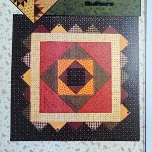 May include: A quilt pattern titled "Squared" by Kansas Troubles Quilters. The design features a central square with a diamond pattern in red, brown, and yellow, surrounded by a black and white patterned border. The designer's name, Lynne Hagmeier, is also visible.
