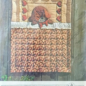 May include: A quilt pattern titled "Puppy Love Quilt" with a fast, fun applique pattern. The quilt features a brown puppy applique with a red bow, surrounded by red heart appliques. The pattern is from "The Gingham Goose" and was designed by Gwen Andrews.