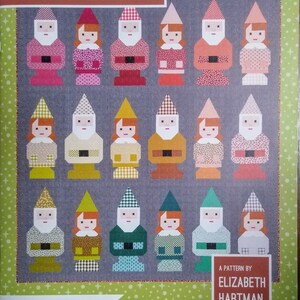 May include: A patchwork quilt pattern titled "Norm & Nanette" featuring a grid of gnome-like figures. The figures have various patterned outfits in shades of pink, red, green, and yellow. The pattern is by Elizabeth Hartman.