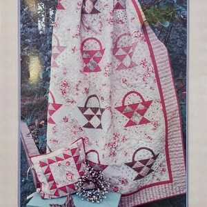May include: A quilt and pillow set with a basket design. The quilt features repeating basket patterns in red and brown on a cream background with floral accents. The pillow has a matching design. The text "Sew Simple Baskets" is at the top.