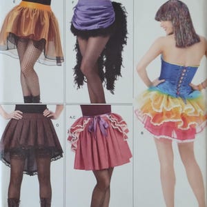 May include: A Simplicity 1346 sewing pattern envelope featuring illustrations of five skirt variations. Designs include a gold high-low skirt, a purple ruched skirt with black feathers, a brown lace-trimmed skirt, a pink skirt with ruffles, and a rainbow corset outfit.