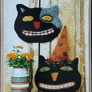 May include: A pattern sheet titled Humble Handwork by American Folk Artist S. West featuring a black cat hooked mat and a black cat pillow with an orange polka dot hat, orange flowers in a striped tin, and text stating 12 inches by 10 inches.