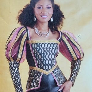 May include: A Renaissance-style costume featuring a black bodice with a gold and white pattern, accented with gold trim. The sleeves are pink and gold, with black and gold patterned cuffs. The costume has a square neckline and puffed sleeves.