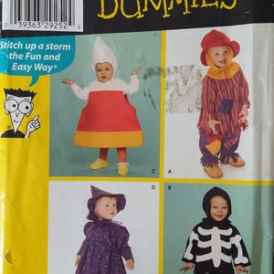 May include: A Simplicity Sewing Patterns for Dummies envelope featuring four toddler costume designs: a white, orange, and yellow candy corn outfit, a colorful striped scarecrow with a red hat, a purple star-patterned witch, and a black skeleton suit.