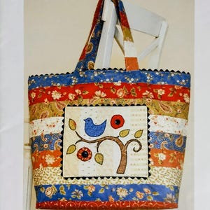 May include: A colorful patchwork Jelly Roll Bag with a bird and tree applique. The bag features a variety of patterned fabrics in red, blue, orange, and cream. The bag measures 17" x 17" x 7". The text "Jelly Roll Bag" is at the top.