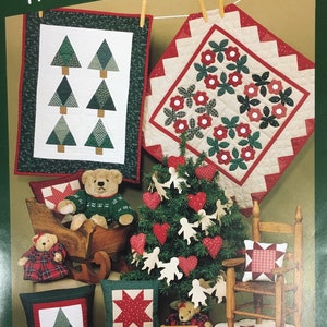 May include: A Christmas-themed image featuring various quilted items. Includes two small quilts, pillows, a Christmas tree with heart and angel ornaments, teddy bears, and a small wooden chair. The text "Christmas The Little Quilt Collection" is at the top.