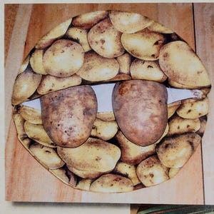 May include: A whimsical artwork featuring a potato-themed design. The image showcases a circular arrangement of small, light-brown potatoes, forming the outline of a face. Two larger potatoes are positioned to resemble eyes, creating a playful and unique composition.
