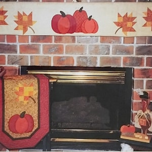 May include: A fall-themed fireplace mantel with a decorative valance featuring pumpkins and maple leaves. A matching table runner with a pumpkin and leaf design is on the hearth. A teddy bear and wooden turkey decoration complete the autumn decor.