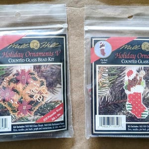 May include: Two Mill Hill Holiday Ornaments V counted glass bead kits. One kit features a poinsettia wreath design, the other a stocking teddy design. Both kits include glass beads, floss, needles, and instructions.