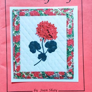 May include: A craft pattern titled "Petal Play" featuring a geranium design. The artwork includes a red flower, dark green leaves, and the text "GERANIUM - #101". The dimensions are 14" x 16".