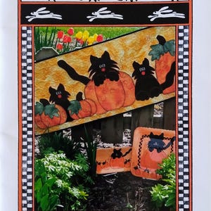 May include: A decorative print titled "The Pottery Collection Pumpkin Patch" featuring black cats and orange pumpkins. The border includes carrots, green leaves, and white rabbits. The text "Table Quilts by Rabbit Run" is at the bottom.