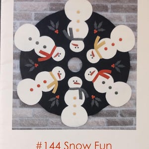May include: A circular black tree skirt with white snowman designs, each adorned with colorful scarves and button details. The text "Button Stitch Designs" and "#144 Snow Fun" are visible. The tree skirt has a 36-inch diameter.