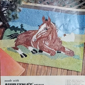 May include: A vintage punch needle rug foundation kit with the word "PASTORAL" at the top. The design features a brown and white horse lying on a green field with a blue sky background. Finished size is 34 x 48 inches.