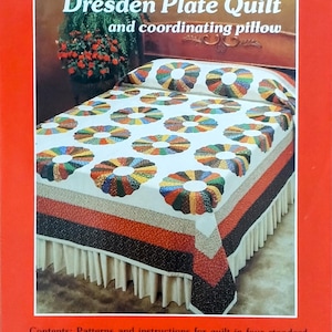 May include: A red book cover with the text "A Quilt Pattern and Instructions by Yours Truly" and "Dresden Plate Quilt and coordinating pillow." The image shows a quilt with colorful circular patterns on a white background. The quilt is on a bed with a matching pillow.
