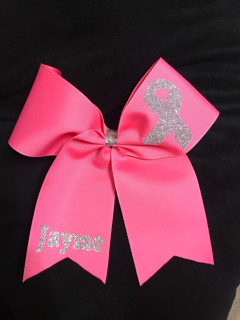May include: Pink cheer bow with a silver glitter ribbon and the name "Jayme" in silver glitter.