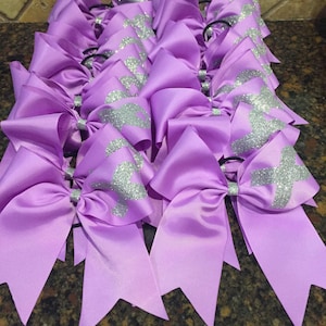 May include: A group of purple hair bows with silver glitter accents. The bows are tied with black elastic hair ties.