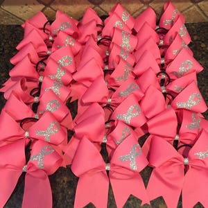 May include: A group of pink cheer bows with silver glitter ribbons. The bows are tied with black elastic bands.