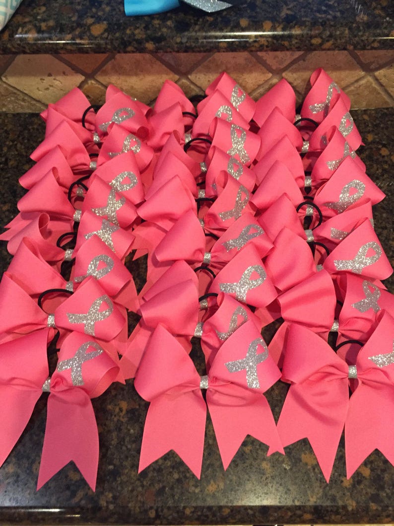May include: A group of pink cheer bows with silver glitter ribbons. The bows are tied with black elastic bands.