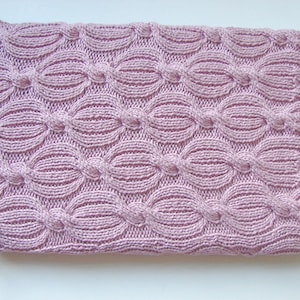 Op de afbeelding: Een zacht, roze gebreid deken met een kabelbreipatroon.