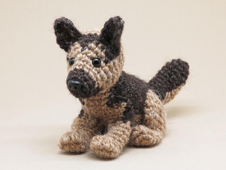 K&ouml;nnte beinhalten: Ein geh&auml;keltes Stofftier in Form eines Hundes mit braunem und braunem Fell. Der Hund sitzt mit den Beinen unter dem K&ouml;rper und dem Schwanz hinter sich eingerollt.