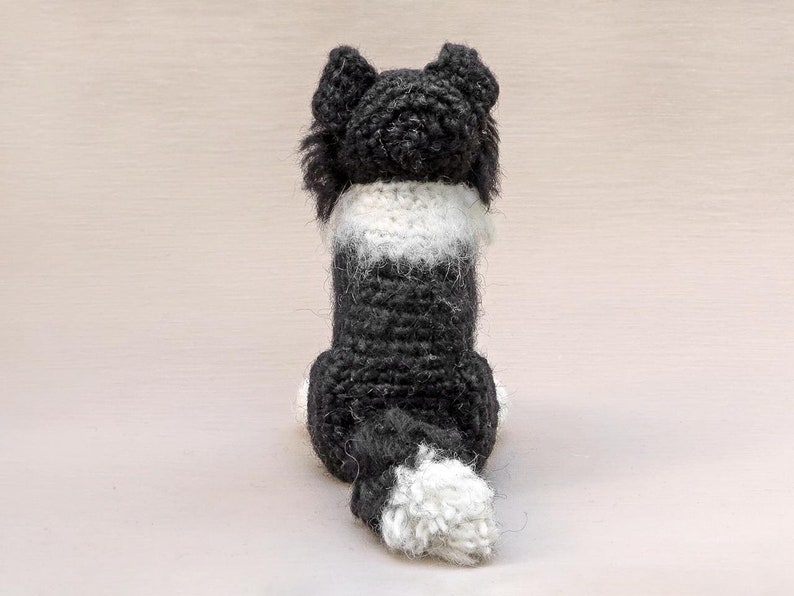 May include: A black and white crocheted dog toy with a fluffy tail. The dog is sitting with its back to the camera.