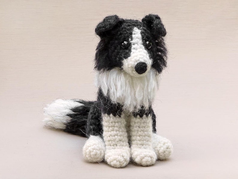 May include: A crocheted black and white border collie dog toy. The dog is sitting with its paws in front of it. The dog has a fluffy white tail.