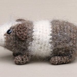 May include: A brown and white crocheted guinea pig toy with black eyes. The toy is made with soft, fuzzy yarn and has a realistic appearance.