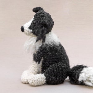 May include: A crocheted black and white border collie dog sitting with its tail curled behind it. The dog is made of yarn and has a fluffy white chest and tail.