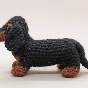 May include: A black and brown crocheted dachshund toy. The toy has a long body, short legs, and a long tail.