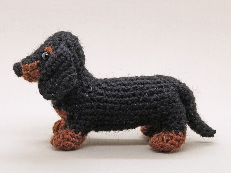 May include: A black and brown crocheted dachshund toy. The toy has a long body, short legs, and a long tail.